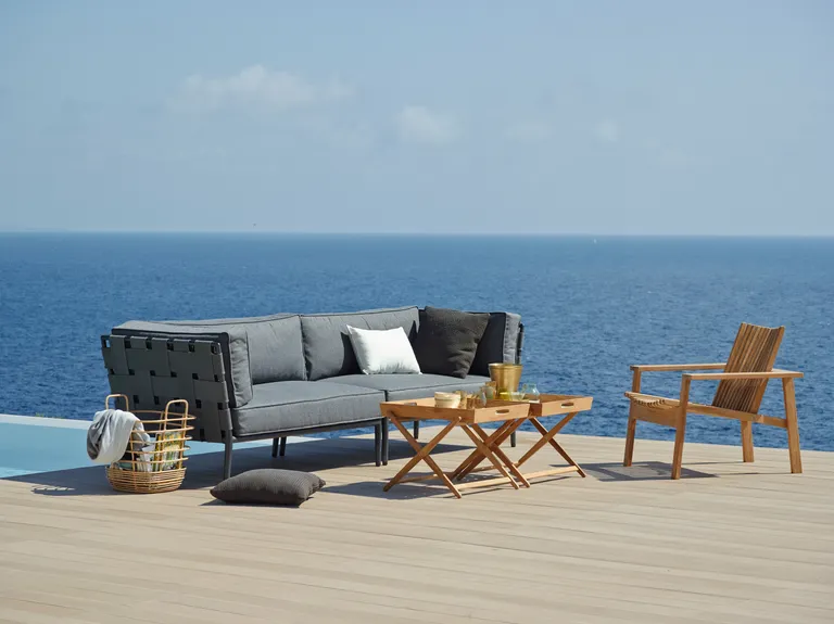 Modernes Outdoor-Sofa in Grau auf einem Balkon, im Hintergrund ist Meer zu sehen.