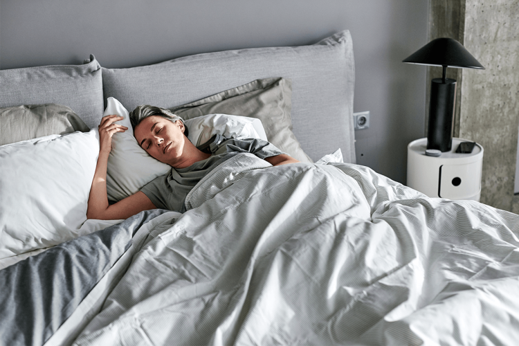 Frau liegt in einem Bett mit gemütlicher Bettwäsche und schläft.