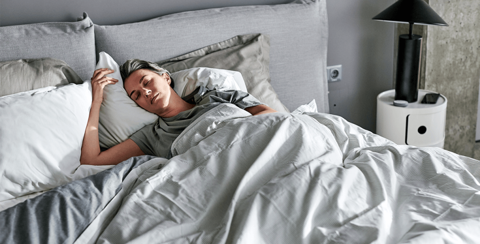Frau liegt in einem Bett mit gemütlicher Bettwäsche und schläft.