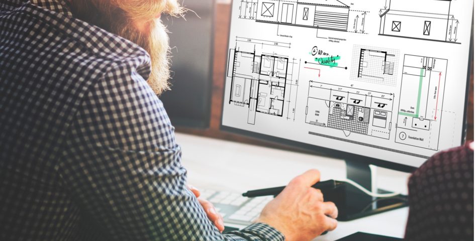 Mann mit Bart sitzt vor einem Computer und plant digital den Umriss eines Hauses.